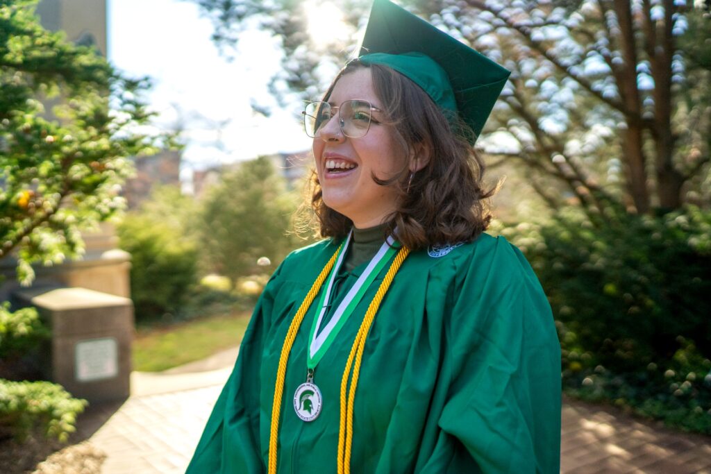 Portrait of someone in a graduation gown laughing outdoors.