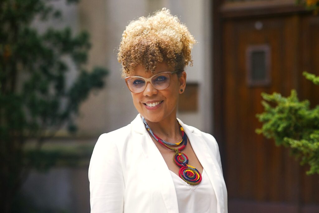 Woman smiling were glasses and an all-white outfit with a brightly colored necklace.